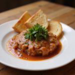 Delicious plate of Tartar De Fuet garnished with parsley and served with toasted bread.