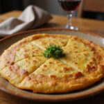 Tortilla de patatas recién hecha en un plato cerámico para receta de tortilla de patatas, acompañada de vino tinto.