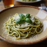 Espaguetis al pesto servidos con albahaca y queso parmesano en un plato rústico.