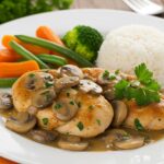 Pechugas de pollo en salsa de champiñones servidas con arroz y verduras al vapor para una cena deliciosa.
