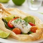 Pescado blanco al papillote servido con rodajas de lima y verduras, ideal para una cena saludable.