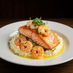 Plato de salmón y camarones cremosos a la toscana sobre puré de patatas, ideal para disfrutar.