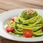 Plato final de zoodles de calabacín con pesto ligero, tomates cherry y piñones, perfecto para recetas saludables.