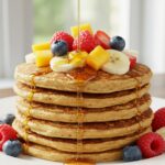 Deliciosos panqueques de alta proteína servidos con fruta fresca y jarabe.