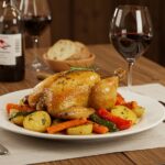 Plato de pollo a l'ast valenciano servido con verduras asadas y vino, perfecto para una cena.