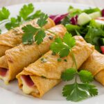 Rollitos de pollo rellenos de jamón y queso perfectamente presentados con guarnición.