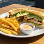Sándwich de pollo derretido con aguacate y papas fritas, ideal para una comida deliciosa.