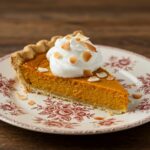 PorciĂłn de tarta de calabaza y coco sin gluten decorada con crema batida y coco tostado.