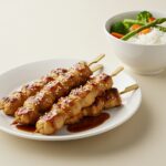 Yakitori de pollo terminado con salsa teriyaki, acompañado de arroz y verduras al vapor, ideal para cenas.