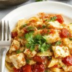 A vibrant plate of ensalada de pasta con pollo featuring colorful pasta, tender strips of chicken, cherry tomatoes, green herbs, and a sprinkle of cheese on a white plate, garnished with fresh herbs, with a bright, summery background.