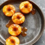 A close-up of shiny white caramel apples coated with a glossy glaze, decorated with elegant drizzles and tiny sparkles, arranged on a sophisticated platter with soft lighting highlighting their smooth texture and shimmering finish.