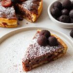 A sliced pastel de chocolate con moras on a elegant white plate, revealing its moist, layered interior filled with dark chocolate and fresh blueberries, topped with a dusting of powdered sugar and a few whole berries for garnish. The cake's rich brown hue contrasts beautifully with the vibrant blue of the berries, highlighting the fruity and chocolaty combination.