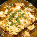 Plato de pollo al ajo y parmesano en crockpot, con pollo dorado y grueso cubierto con queso parmesano rallado, rodeado de trozos de ajo y hierbas, en un plato blanco elegante sobre una mesa rústica.