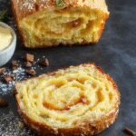 Un pan de calabacín esponjoso y dorado en un plato blanco, con una corteza suave y ligeramente crujiente. La miga interna muestra pequeñas burbujas y trozos de calabacín visible, con un aroma tentador en un ambiente acogedor.