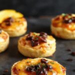 Delicadas trufas de color naranja y crema, cubiertas con una fina capa de cacao en polvo, presentadas en un plato blanco sobre una mesa de madera, rodeadas de trozos de calabaza y queso crema, con una textura suave y apetecible.