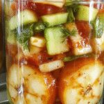 A glass jar filled with colorful vegetables in escabeche resting on a wooden table. Visible are bright orange carrots, green beans, white cauliflower florets, and slices of red bell pepper, all submerged in a golden-yellow vinegar-based brine with herbs. The vegetables appear fresh, crisp, and vibrantly colored, with a glossy sheen from the pickling liquid. The jar is slightly tilted, showcasing the layered arrangement of the vegetables and the herbs floating within.