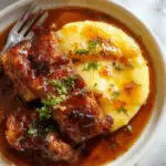 A rustic bowl of rich, dark brown estofado de olla with tender chunks of beef, garnished with fresh herbs, served alongside a creamy, golden polenta de Gorgonzola. The dish is presented on a wooden table with a rustic cloth, emphasizing its hearty, comforting nature and Italian origin.