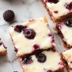 A close-up of blueberry cream cheese bars with a golden-brown crust topped with a vibrant blue blueberry filling and a swirl of cream cheese, garnished with fresh blueberries and a dusting of powdered sugar. The bars are cut into neat squares, revealing layers of crumbly crust, creamy filling, and juicy blueberries, presented on a rustic wooden platter.