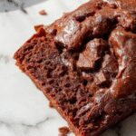 A sliced Chocolate Espresso Banana Bread showcasing its moist crumb with swirls of chocolate and espresso, topped with a dusting of cocoa powder, garnished with banana slices on a rustic wooden platter.