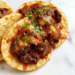 Plato de tacos de birria mexicanos con carne jugosa y tostada, servidos en tortillas doradas y curvadas, acompañados de cilantro y cebolla fresca, con un tazón de consomé caliente a un lado, todo presentado sobre una tabla de madera rústica.