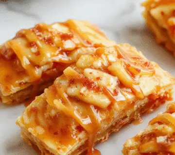 Barritas de manzana con caramelo salado perfectamente horneadas en una bandeja, con un dorado crujiente en la parte superior y un relleno jugoso de manzana visible. La superficie muestra un glaseado de caramelo salado que brilla bajo la luz, con trozos de manzana y un toque de sal en la superficie. La presentación es sencilla pero apetitosa, mostrando las barritas cortadas en porciones individuales, revelando una textura tierna y con un crujiente exterior dorado.