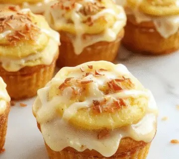 Close-up of golden-brown cupcakes topped with a swirl of cinnamon-spiced apple filling, garnished with a dusting of powdered sugar and cinnamon. The cupcakes are arranged on a rustic wooden tray, with some sliced apple pieces and cinnamon sticks in the background, evoking a cozy autumn atmosphere. The textures of the moist cupcake crumb and glossy apple filling are visually appealing.