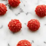 Un cuenco grande de palomitas de maíz de terciopelo rojo contrastando con un fondo oscuro, las palomitas tienen una textura aterciopelada y un resplandor rojo intenso, con algunas dispersas en la mesa que reflejan la iluminación ténue y misteriosa de Halloween.