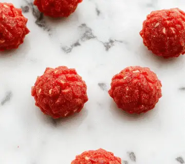 Un cuenco grande de palomitas de maíz de terciopelo rojo contrastando con un fondo oscuro, las palomitas tienen una textura aterciopelada y un resplandor rojo intenso, con algunas dispersas en la mesa que reflejan la iluminación ténue y misteriosa de Halloween.