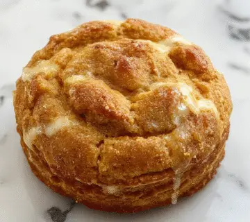 A close-up of a golden-brown pumpkin snickerdoodle bread loaf topped with a generous sprinkling of cinnamon sugar, with a slightly cracked surface revealing a moist, spiced interior. The bread is sliced open to display its soft crumb and tender texture, with warm hues of orange and cinnamon. The loaf is presented on a rustic wooden board, accented with cinnamon sticks and a few pumpkin seeds.