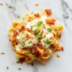 Un plato hondo de pasta cremosa con trozos de pollo dorado, crujiente tocino y un toque de hierbas verdes, todo cubierto con una salsa blanca suave y apetitosa, presentado sobre un fondo neutro con algunos ingredientes dispersos
