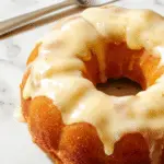 Un hermoso pastel Bundt de calabaza de color naranja vibrante con una textura suave, decorado con especias y una pizca de azúcar glas en la parte superior. El pastel está en una bandeja de pastel moderna con un fondo neutro, resaltando su presentación apetecible y otoñal.