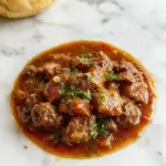 Un plato de ragú de carne de res en una cacerola, con carne tierna y salsa espesa, adornado con hierbas frescas y servido sobre pasta o acompañado de verduras. La carne se ve jugosa, con trozos grandes y bien cocidos, con un rico color marrón profundo y una textura suave. La presentación muestra el ragú en un plato rústico, resaltando su consistencia cremosa y apetitoso acabado.