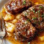 Un plato de Salisbury Steak con albóndigas doradas cubierto con una rica salsa marrón, acompañado de verduras y puré de papas, presentado en un plato rústico de cerámica en una mesa acogedora con fondo desenfocado, resaltando la textura jugosa de la carne y la salsa brillante.