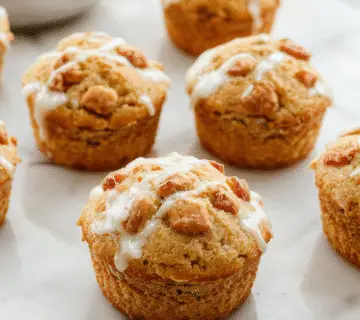 Un plato de muffins de pera especiada apilados en un plato blanco sobre una mesa de madera, con algunas peras frescas y especias como canela y nuez moscada dispersas alrededor. La corteza dorada y la textura esponjosa de los muffins son claramente visibles, con pedazos de pera en su interior. La presentación es acogedora y otoñal, con un fondo suave y cálido que realza los tonos cálidos de los muffins y las peras.