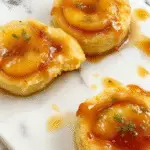 Un pastel de volcán de manzana y caramelo en una olla de cocción lenta, mostrando capas doradas de manzana caramelizada cubiertas con un glaseado brillante, decoradas con rodajas de manzana y una pizca de canela, todo en un plato rústico sobre una mesa de madera.